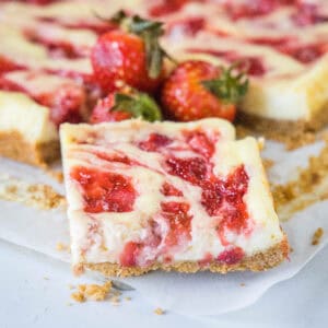 Close up of a strawberry cheesecake bar with fresh strawberries and more bars in the background.