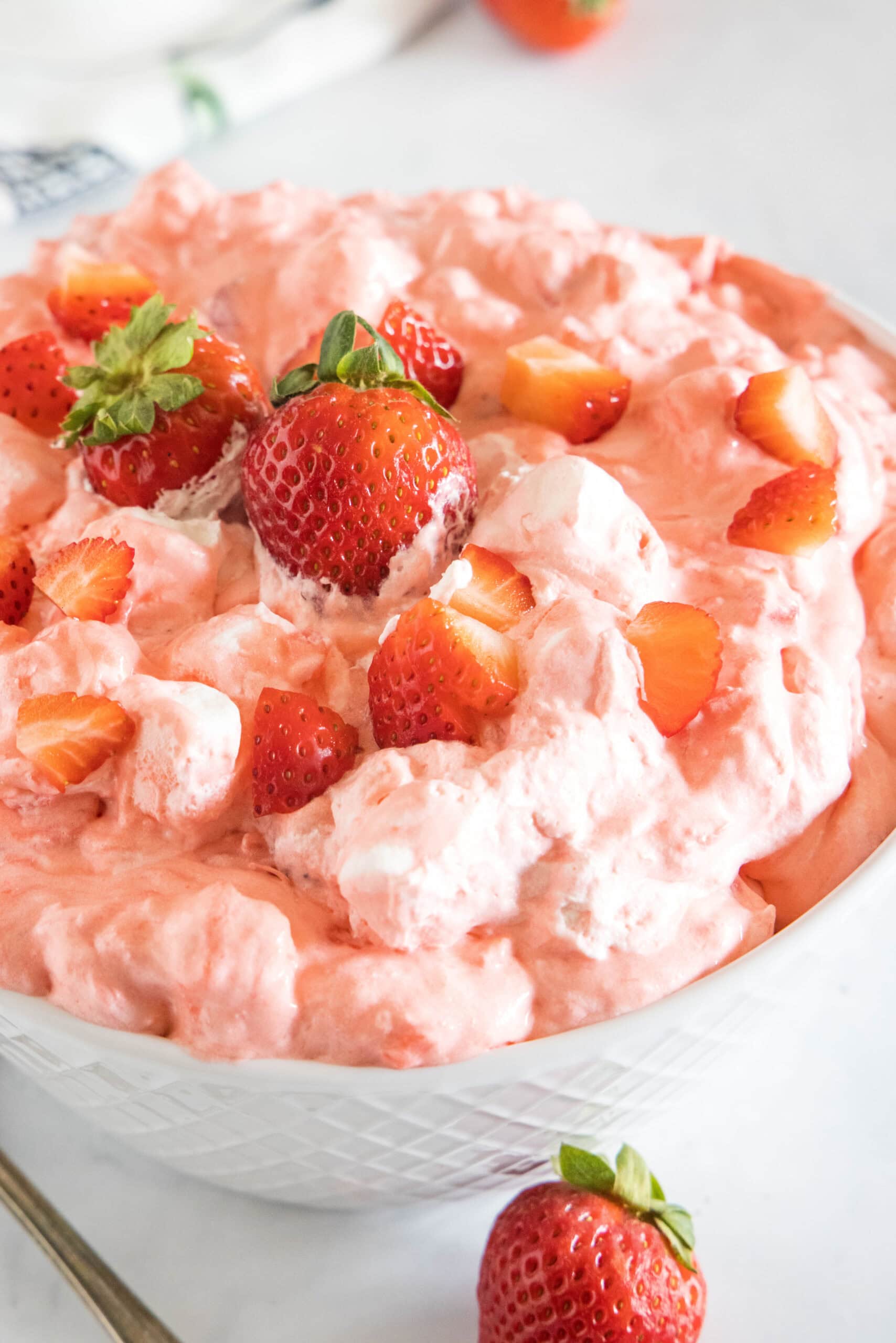 This easy strawberry fluff is a light and creamy dessert salad that's perfect for summer. Fluffy, sweet, and filled with fresh strawberries! Strawberry fluff topped with chopped strawberries in a white bowl.