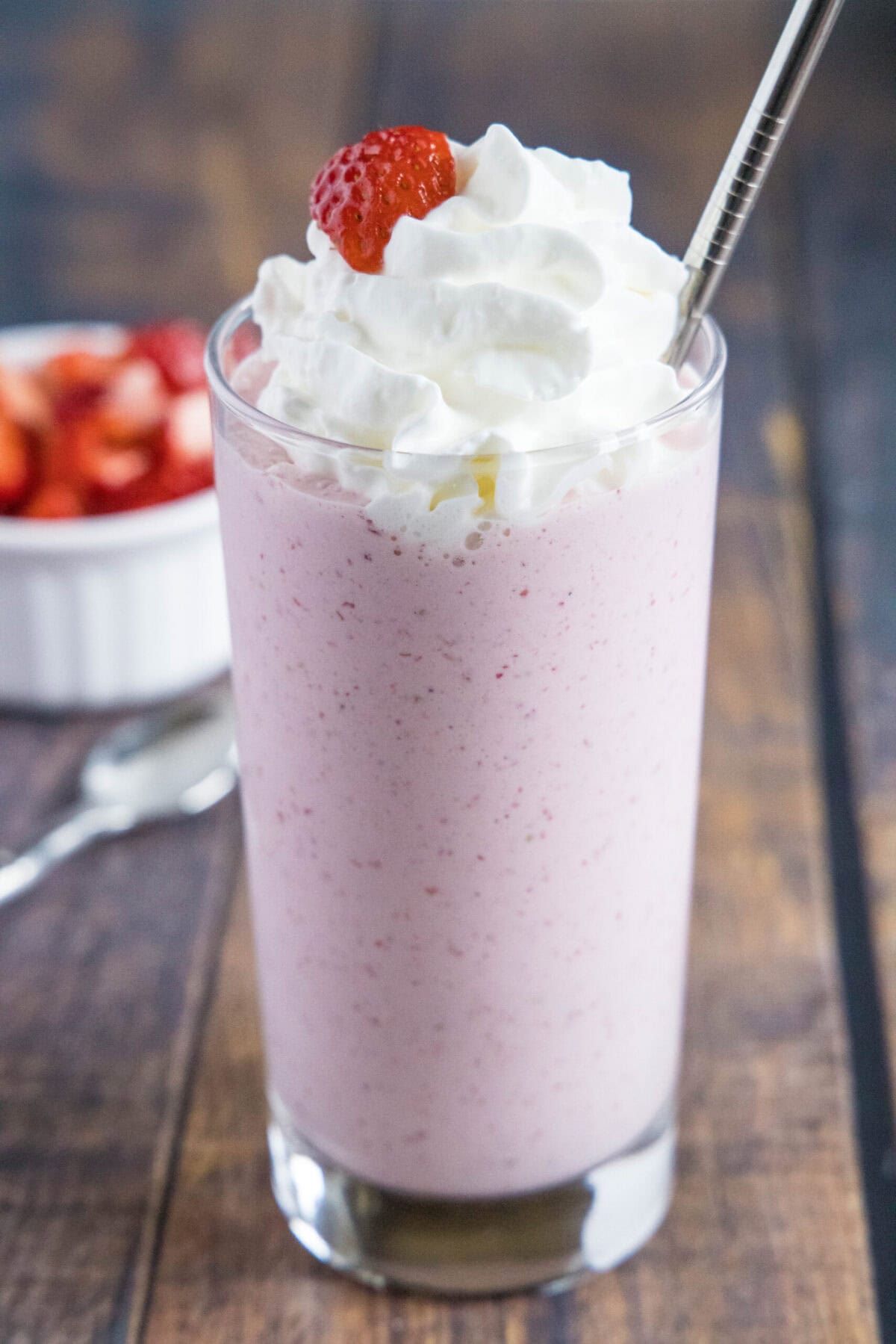 These 5-ingredient strawberry milkshakes are full of nostalgia and flavor. They're quick and easy to make, and absolutely delicious. Close up of a glass of strawberry milkshake with whipped cream, a strawberry garnish, and a straw