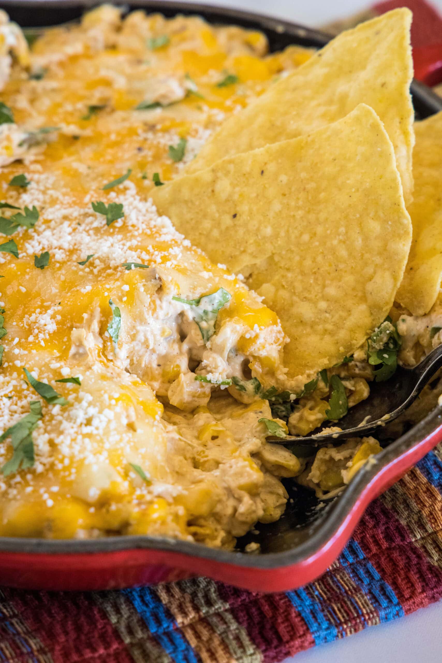 This creamy Mexican street corn dip is an easy recipe filled with charred sweet corn, hot melty cheeses, chili, and lime. Perfect for parties! A tortilla chip dipped into a skillet of cheesy street corn dip.