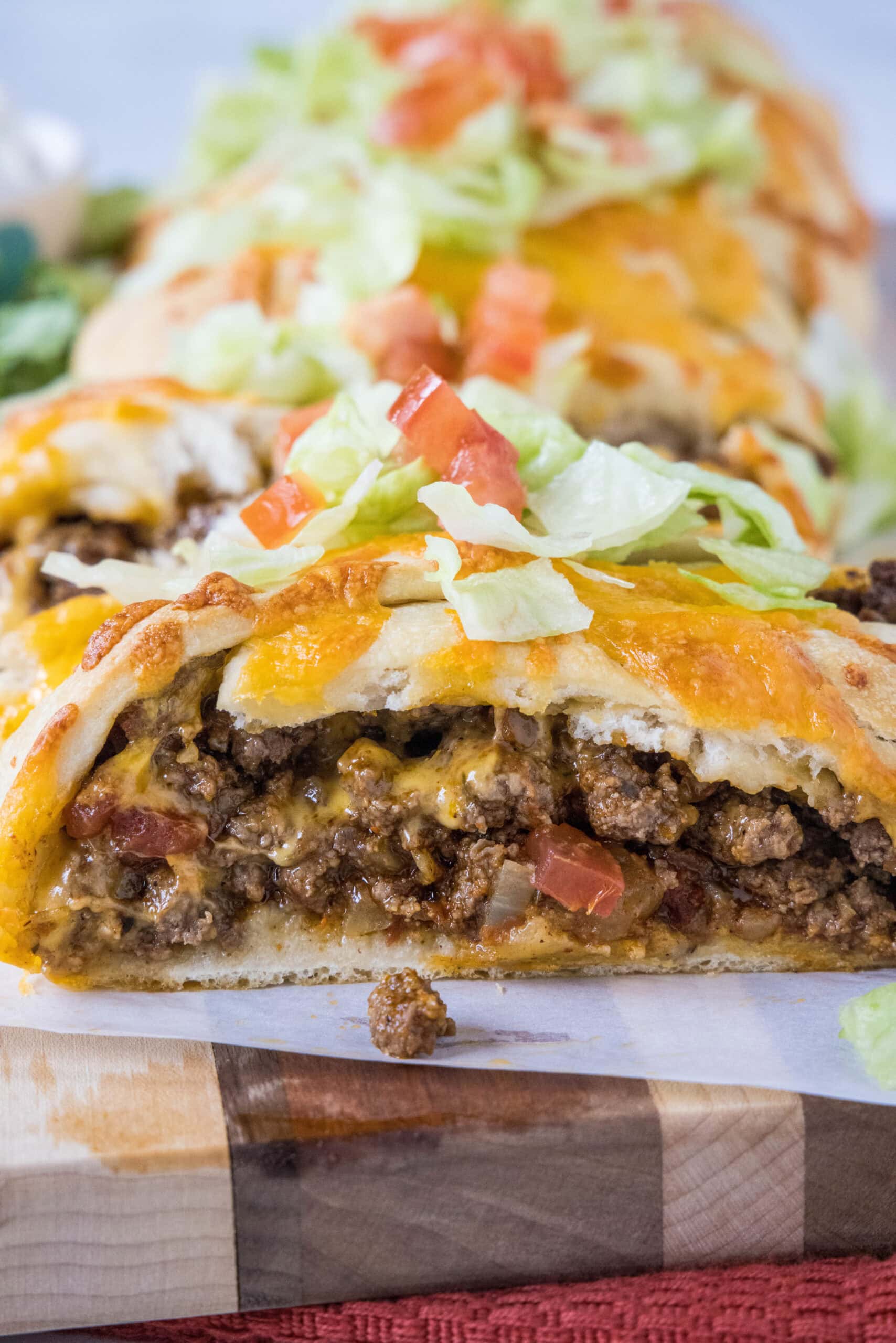 Put a twist on taco night with this easy taco braid! A fun appetizer made from pizza dough and your favorite toppings. Just fill, fold, bake! Close up of a taco braid filled with ground beef and topped with melted cheese, shredded lettuce, and diced tomatoes.