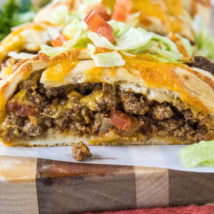 Close up of a taco braid slice filled with ground beef and topped with melted cheese, shredded lettuce, and diced tomatoes.
