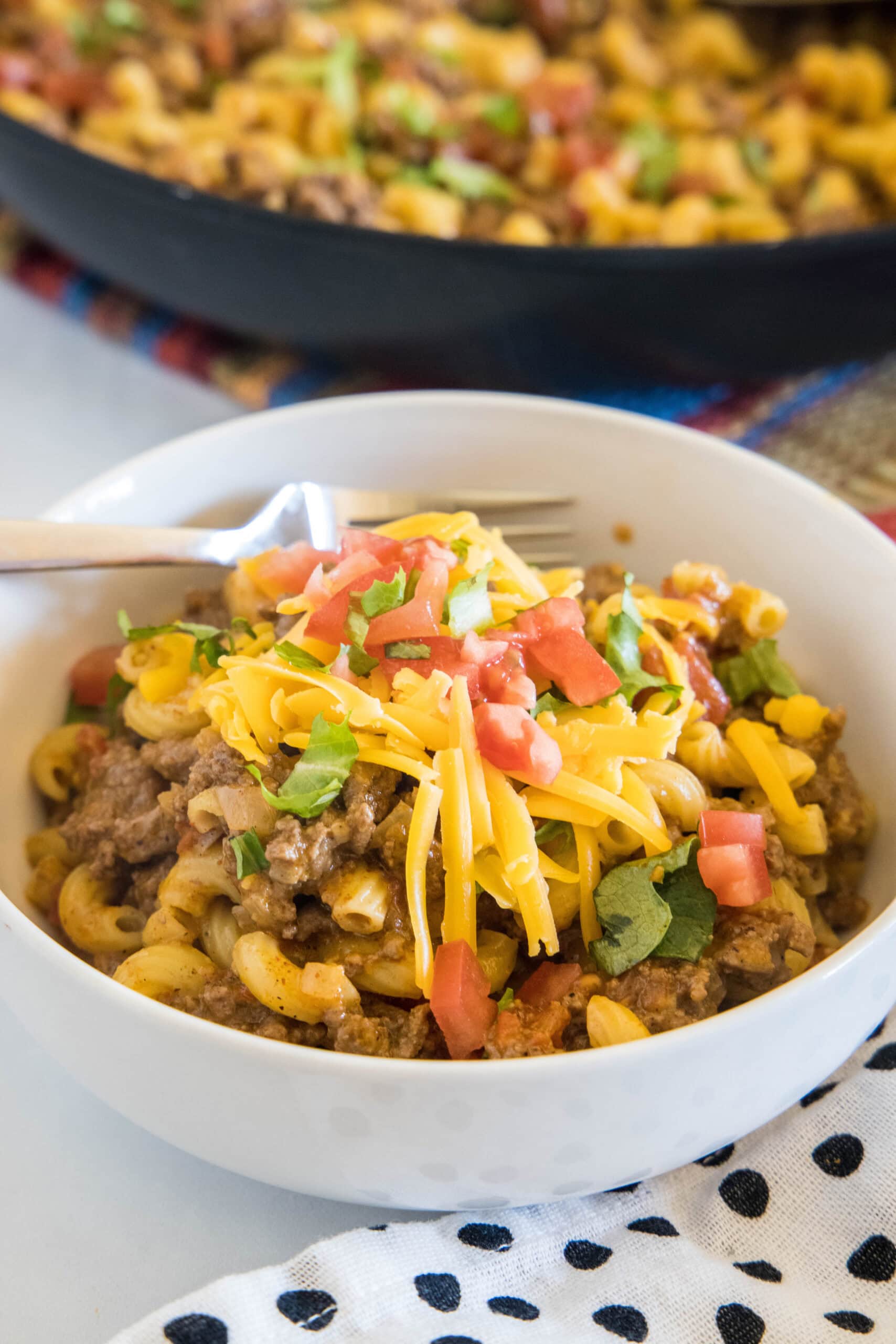 This easy taco mac and cheese recipe combines two favorite comfort foods into one cheesy, flavor-packed skillet dinner! A bowl of taco mac and cheese with a skillet in the background.