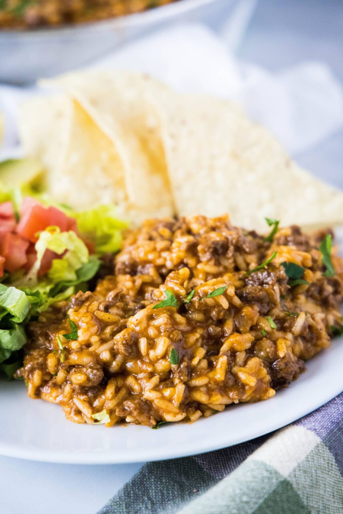 This easy taco rice recipe is full of juicy, seasoned beef, and melty cheddar cheese. It's an easy weeknight Mexican meal. A plate with taco rice, topped with lettuce and cilantro, with tortilla chips on the side