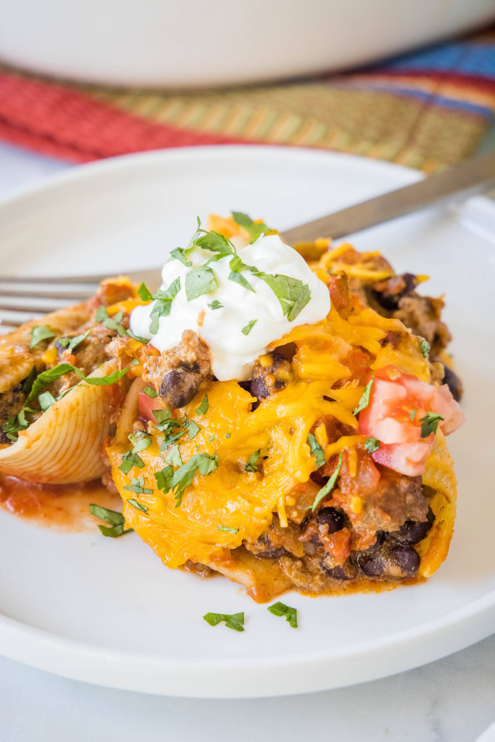 Cheesy taco stuffed shells are an easy Tex-Mex dinner made from jumbo pasta shells filled with creamy taco beef, salsa, and melty cheese. A serving of taco stuffed shells on a white plate next to a fork.