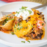 A serving of taco stuffed shells on a white plate next to a fork.