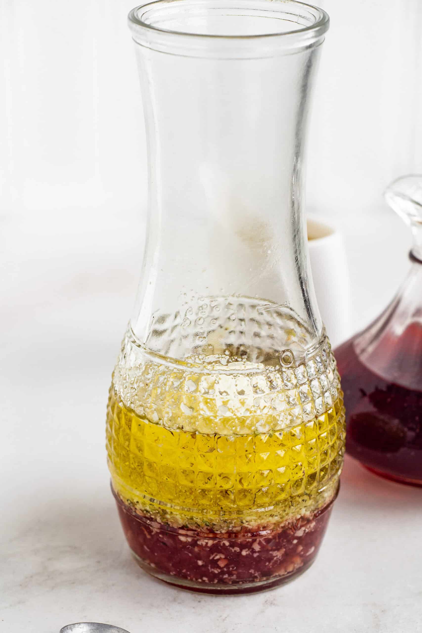 This quick red wine vinaigrette needs 6 ingredients, including olive oil, red wine vinegar, and herbs. It's great on salads and sandwiches! Red wine vinaigrette ingredients inside a glass carafe.