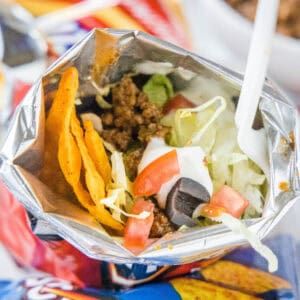 A walking taco topped wth lettuce, tomatoes, and sour cream inside a chip bag with a fork.
